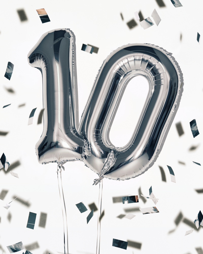 Stříbrné fóliové balony ve tvaru čísla 100 se šňůrkami, obklopené konfety.